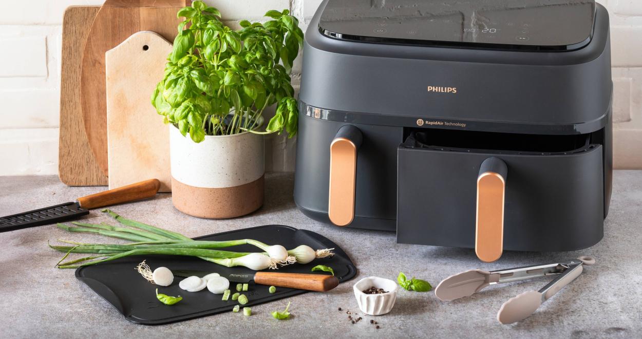 Airfryer auf einer Küchenzeile mit Frühlingszwiebeln auf einem Schneidbrett.