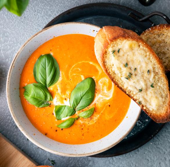 Geröstete Tomatensuppe mit Basilikum und Baguette in Schüsseln.