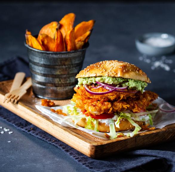 Chicken-Burger mit Süßkartoffelpommes angerichtet auf einem Holzbrett