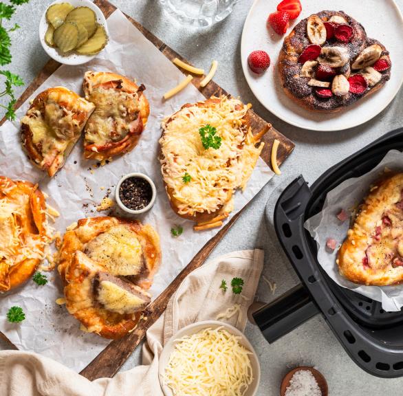 Verschieden getoppte Laugenbrezeln auf einem Tisch neben einer Heißluftfritteuse