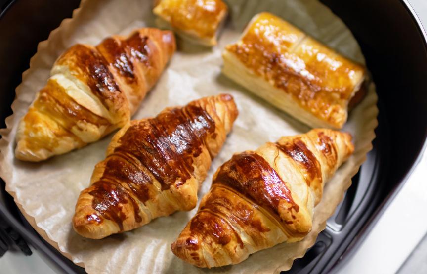 Selbst gebackene Croissants und Pasteten auf einem Stück Backpapier in der Schublade einer Heißluftfritteuse