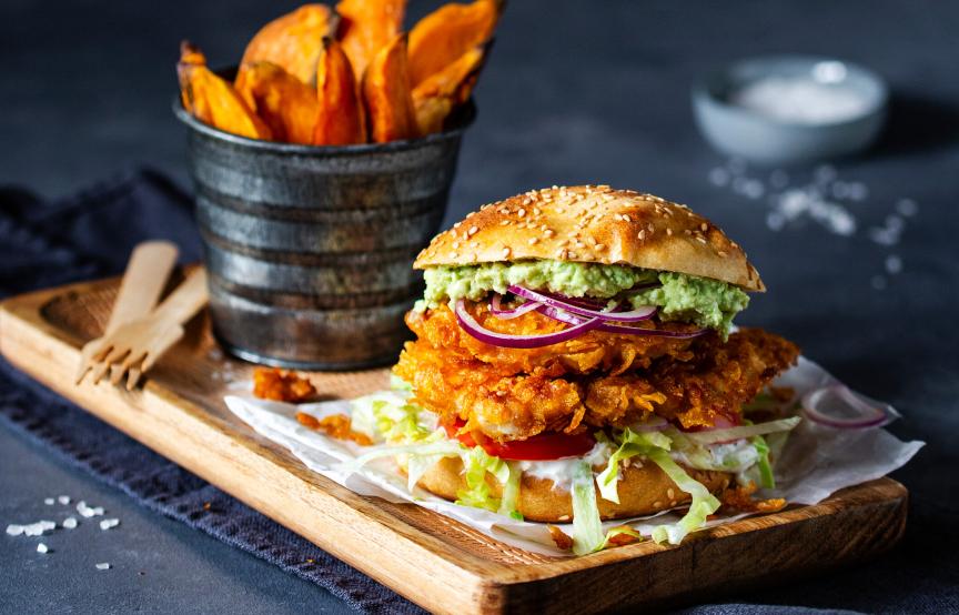 Chicken-Burger mit Süßkartoffelpommes angerichtet auf einem Holzbrett