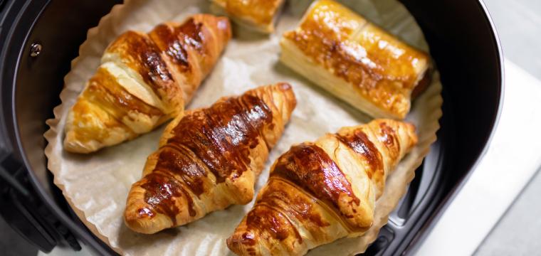 Selbst gebackene Croissants und Pasteten auf einem Stück Backpapier in der Schublade einer Heißluftfritteuse Selbst gebackene Croissants und Pasteten auf einem Stück Backpapier in der Schublade einer Heißluftfritteuse