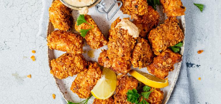 Tofunuggets auf einem ovalen Teller, daneben Cashew-Dip auf einem Tisch Tofunuggets auf einem ovalen Teller, daneben Cashew-Dip auf einem Tisch