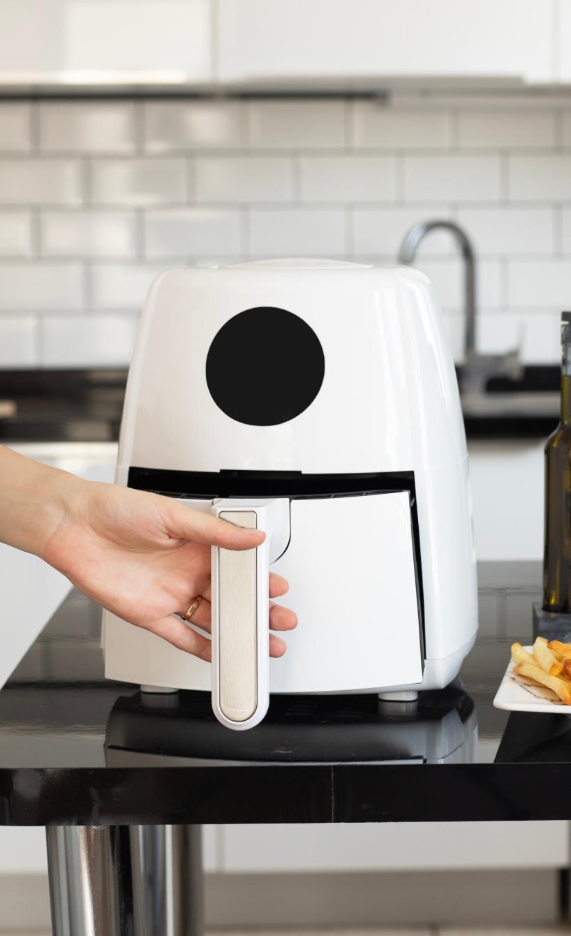 Eine Frau hat ein Baby auf dem Arm und öffnet mit der anderen Hand eine Heißluftfritteuse