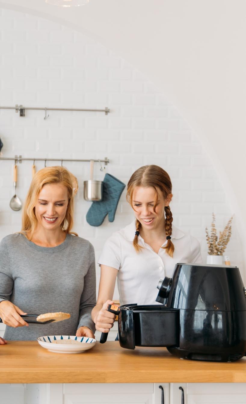 Eine vierköpfige Familie steht um eine Kücheninsel, auf der gerade eine Heißluftfritteuse betätigt wird