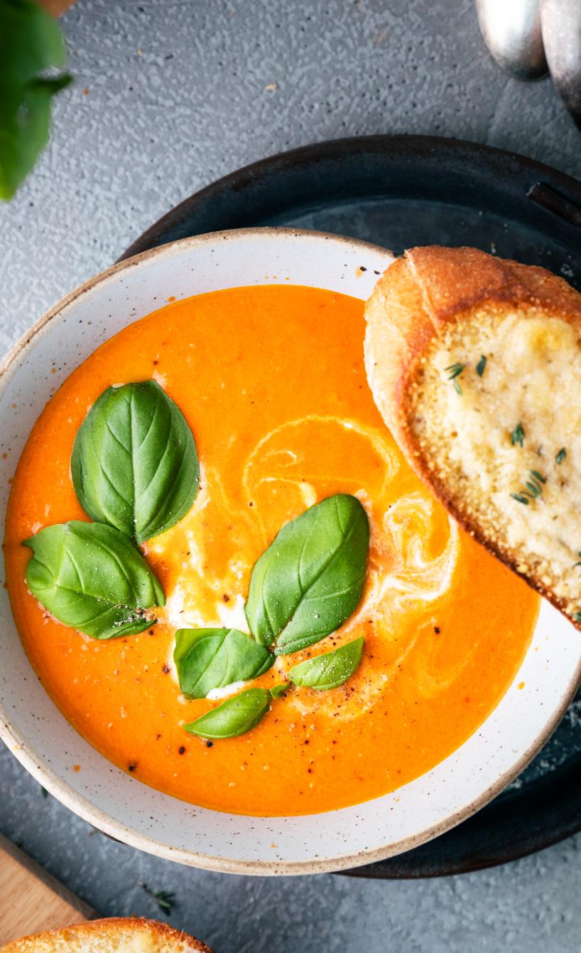 Geröstete Tomatensuppe mit Basilikum und Baguette in Schüsseln.