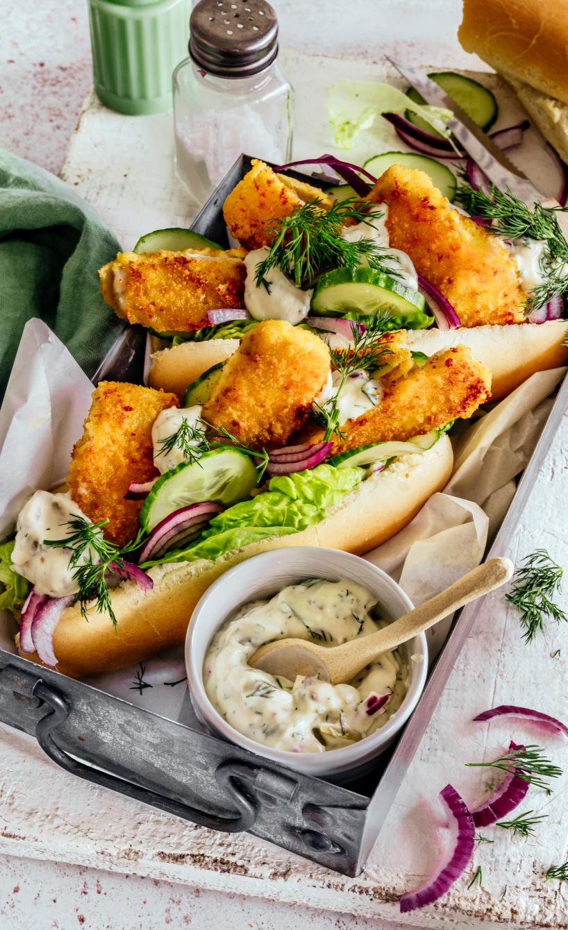 Hot Dogs gefüllt mit Fischstäbchen, Salat und Remoulade auf einem Teller