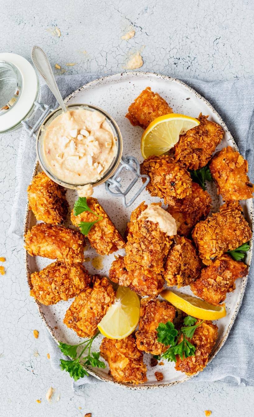 Tofunuggets auf einem ovalen Teller, daneben Cashew-Dip auf einem Tisch