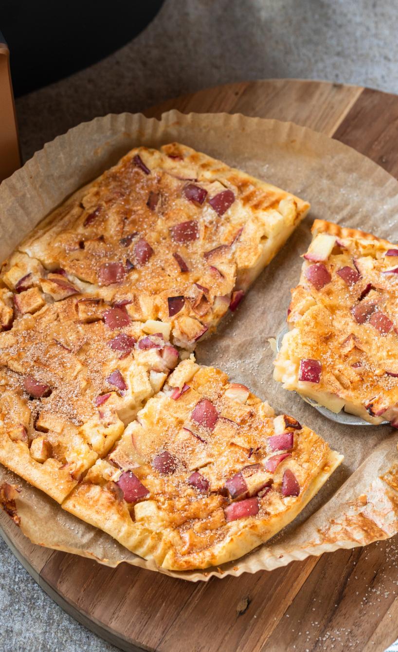 Apfelpfannkucen angeschnitten auf einem runden Backpapierzuschnitt vor einer Heißluftfritteuse