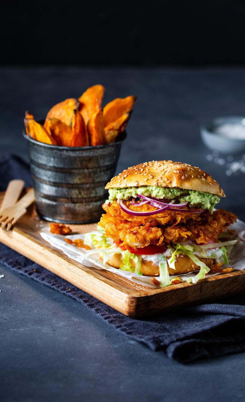 Chicken-Burger mit Süßkartoffelpommes angerichtet auf einem Holzbrett