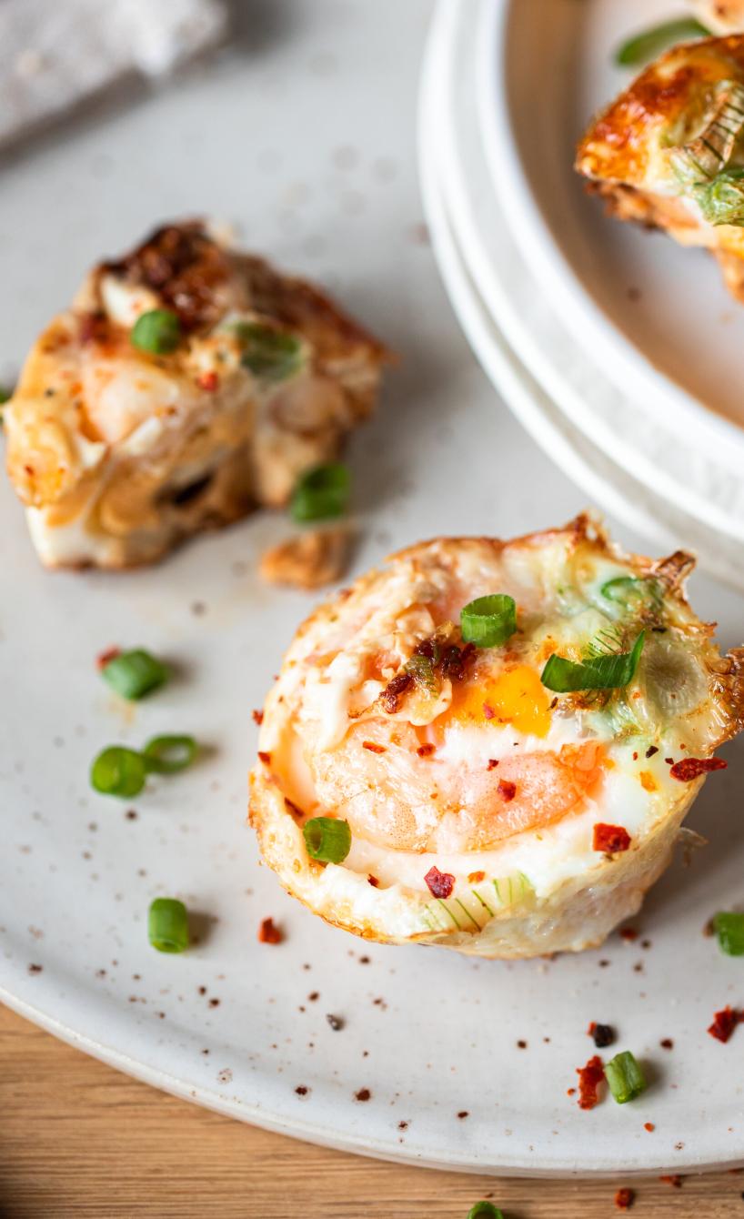 Mehrere Low Carb-Muffins mit Garnelen und Ei getoppt mit frischen Kräutern auf einem Teller
