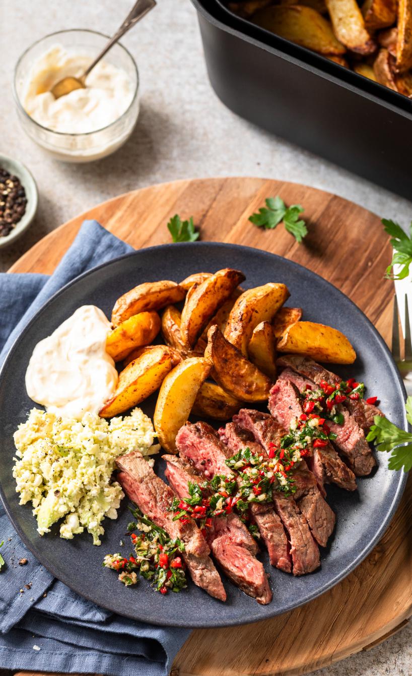 Ribeye-Steak in Scheiben geschnitten mit Kartoffelspalten, Chimichurri und Dips auf einem Teller