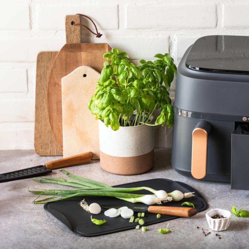 Airfryer auf einer Küchenzeile mit Frühlingszwiebeln auf einem Schneidbrett.