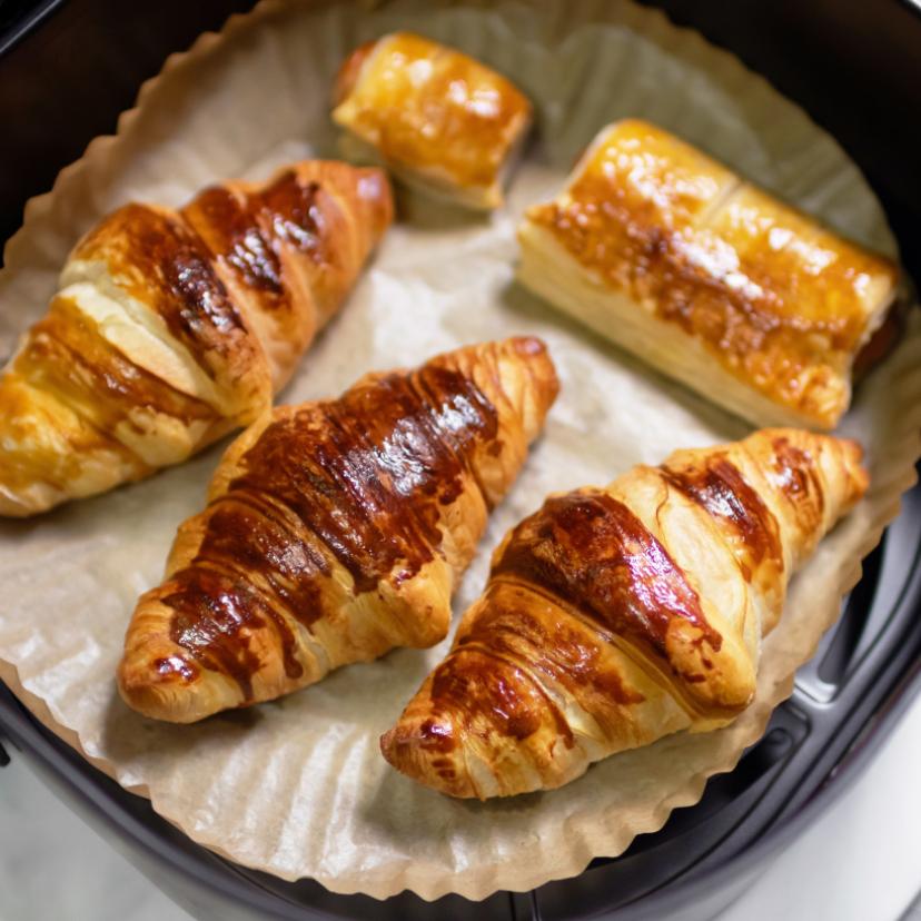 Selbst gebackene Croissants und Pasteten auf einem Stück Backpapier in der Schublade einer Heißluftfritteuse